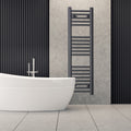 Tall black heated towel rail radiator beside a freestanding bath